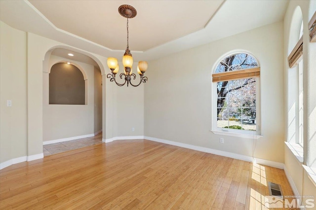 spare room with a tray ceiling, a notable chandelier, and light hardwood / wood-style floors