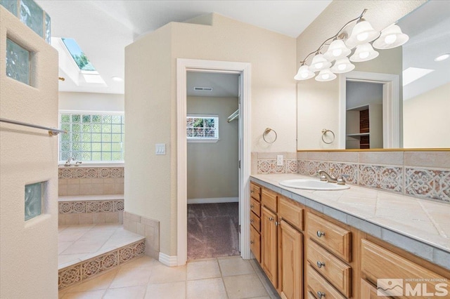 bathroom with a washtub, vaulted ceiling with skylight, vanity, and tile floors