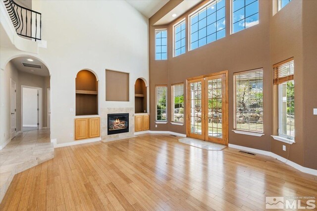 unfurnished living room featuring french doors, a premium fireplace, light hardwood / wood-style flooring, a high ceiling, and built in shelves