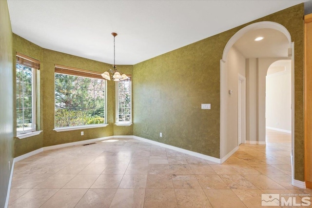 tiled spare room featuring plenty of natural light and an inviting chandelier