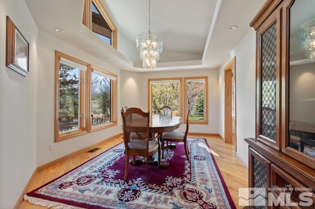 dining room featuring light hardwood / wood-style floors, a chandelier, and a raised ceiling