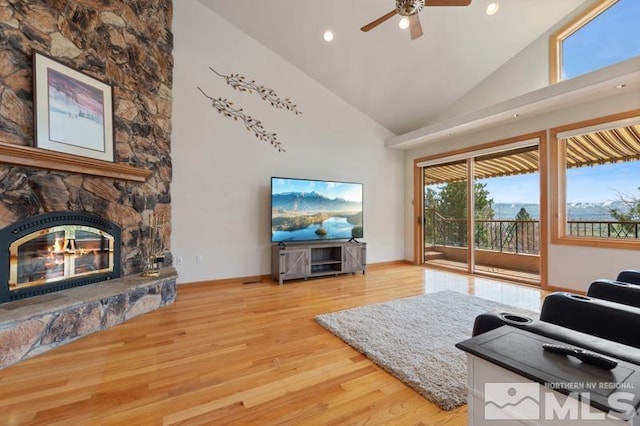 living room featuring light wood-type flooring, ceiling fan, high vaulted ceiling, and a fireplace