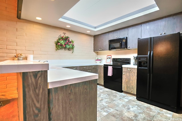 kitchen with sink, a tray ceiling, brick wall, and black appliances