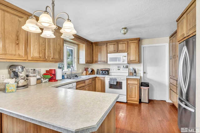 kitchen with sink, decorative light fixtures, white appliances, hardwood / wood-style floors, and an inviting chandelier