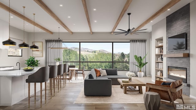 living room with light hardwood / wood-style flooring, beam ceiling, a large fireplace, sink, and ceiling fan