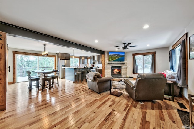 living room featuring ceiling fan with notable chandelier, light hardwood / wood-style flooring, and a fireplace