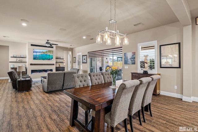 dining space featuring ceiling fan with notable chandelier and dark wood-type flooring