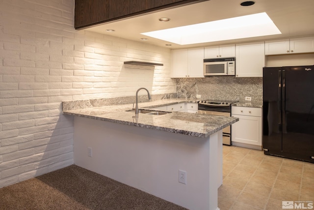 kitchen featuring black refrigerator, brick wall, range with electric cooktop, and sink