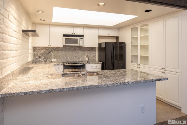 kitchen with white cabinets, black fridge, light stone countertops, sink, and light tile floors