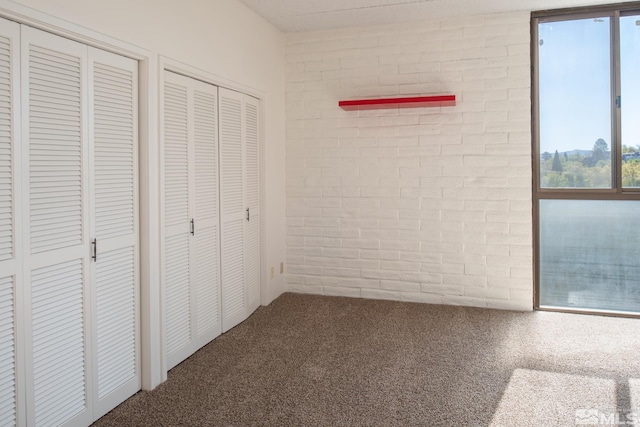 unfurnished bedroom with multiple closets, carpet, and brick wall