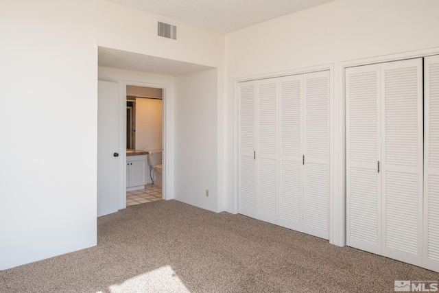 unfurnished bedroom featuring two closets, ensuite bathroom, and carpet flooring