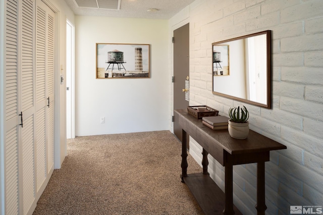 corridor with brick wall, carpet flooring, and a textured ceiling