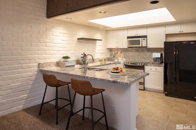 kitchen with brick wall, black refrigerator, stainless steel electric stove, and white cabinets