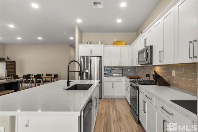 kitchen featuring backsplash, light hardwood / wood-style floors, stainless steel appliances, and a center island with sink