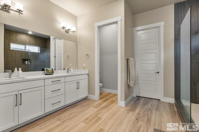 bathroom with wood-type flooring, large vanity, toilet, and dual sinks