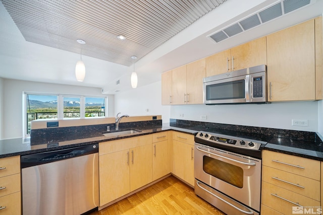 kitchen with hanging light fixtures, light brown cabinets, stainless steel appliances, sink, and light hardwood / wood-style floors