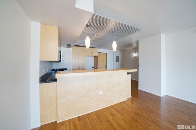 kitchen featuring light brown cabinetry, kitchen peninsula, hardwood / wood-style flooring, and decorative light fixtures