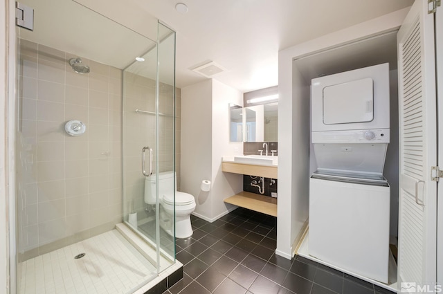 bathroom featuring a shower with shower door, toilet, stacked washer and dryer, vanity, and tile floors