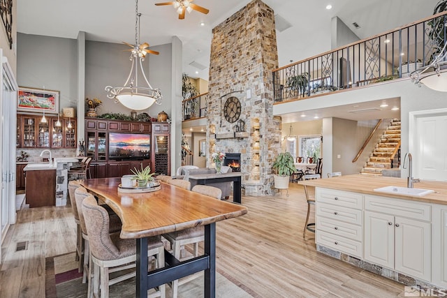 dining area featuring high vaulted ceiling, a stone fireplace, light hardwood / wood-style flooring, ceiling fan, and sink