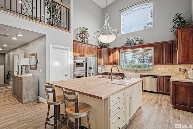 kitchen with wooden counters, backsplash, light wood-type flooring, stainless steel appliances, and a center island with sink