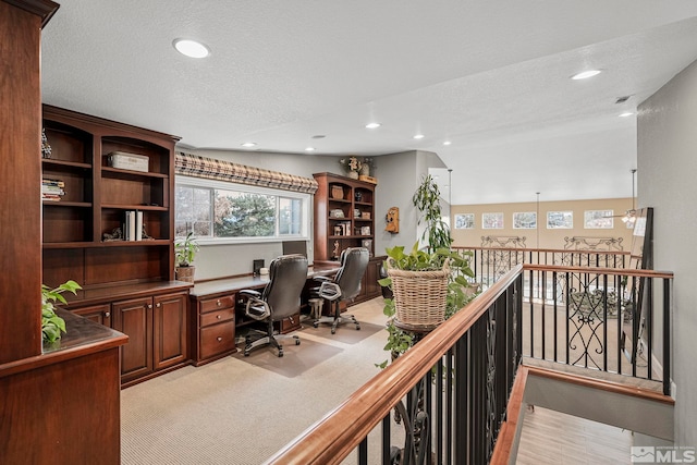 carpeted home office featuring a textured ceiling, built in desk, and vaulted ceiling