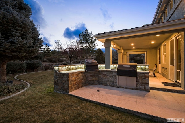 patio terrace at dusk with a yard and exterior kitchen