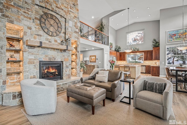 living room featuring a chandelier, a stone fireplace, light hardwood / wood-style floors, and high vaulted ceiling