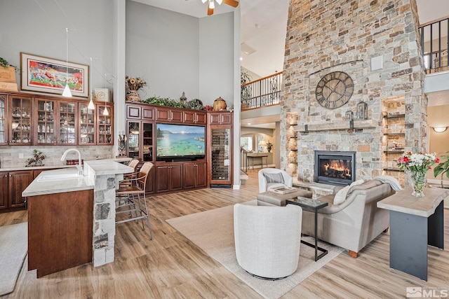 living room featuring a towering ceiling, ceiling fan, light hardwood / wood-style floors, a fireplace, and sink