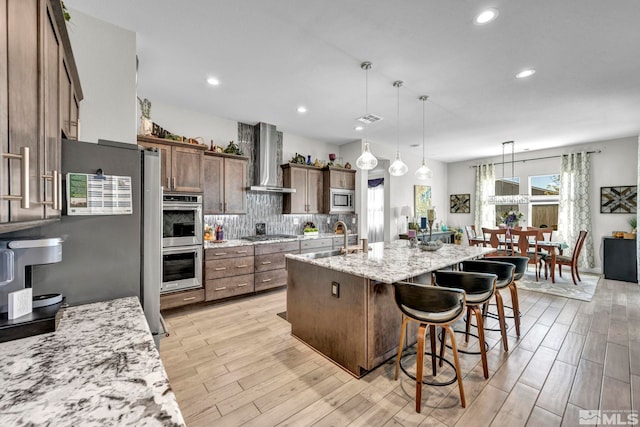 kitchen with decorative light fixtures, light wood-type flooring, backsplash, stainless steel appliances, and a center island with sink