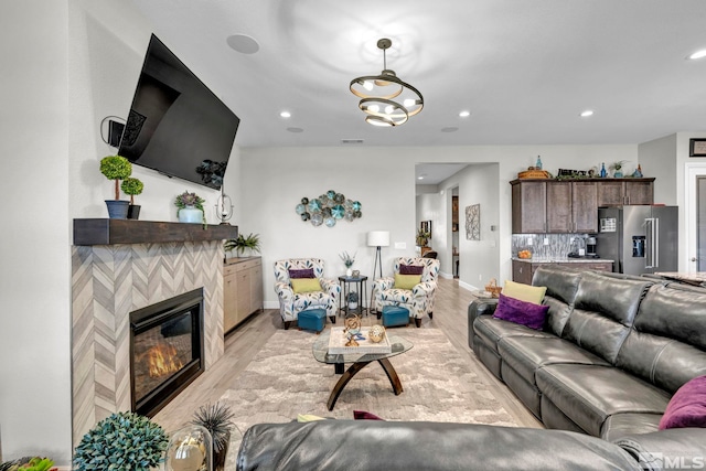 living room with an inviting chandelier, light hardwood / wood-style flooring, and a tiled fireplace