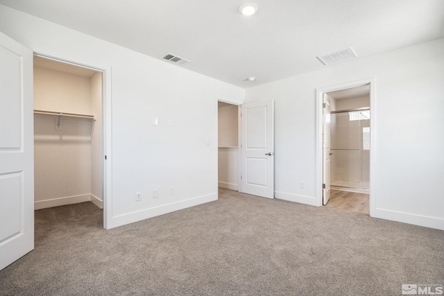 unfurnished bedroom with carpet, ensuite bathroom, a spacious closet, and a closet
