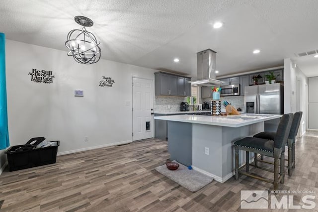 kitchen with island range hood, hardwood / wood-style floors, backsplash, appliances with stainless steel finishes, and a kitchen island