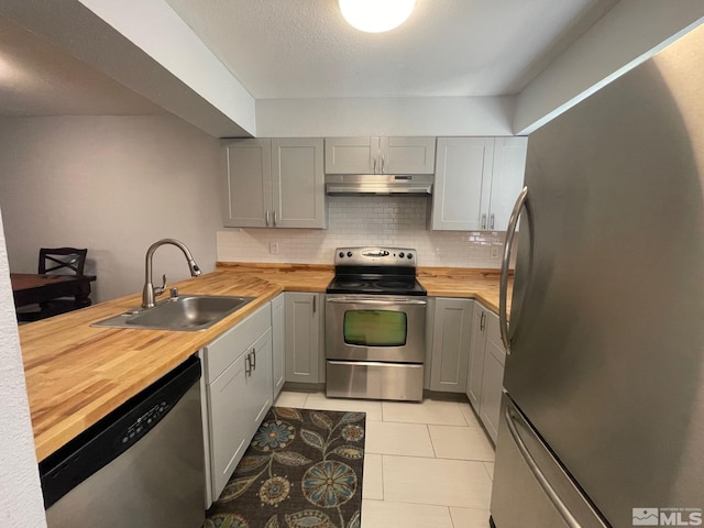 kitchen with tasteful backsplash, light tile flooring, wood counters, sink, and appliances with stainless steel finishes