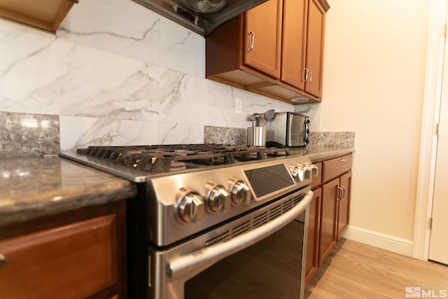 kitchen with light hardwood / wood-style floors, backsplash, high end range, and dark stone counters