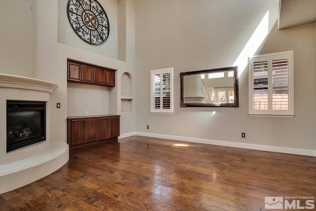 unfurnished living room featuring a towering ceiling and dark hardwood / wood-style floors