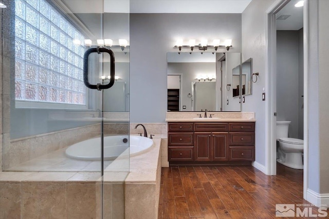 bathroom with oversized vanity, hardwood / wood-style floors, a notable chandelier, a relaxing tiled bath, and toilet