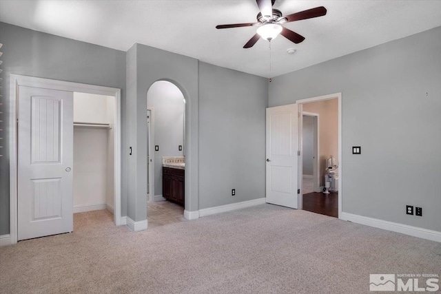 unfurnished bedroom with light colored carpet, connected bathroom, a closet, and ceiling fan