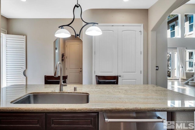 kitchen featuring dark brown cabinets, sink, light stone counters, and decorative light fixtures