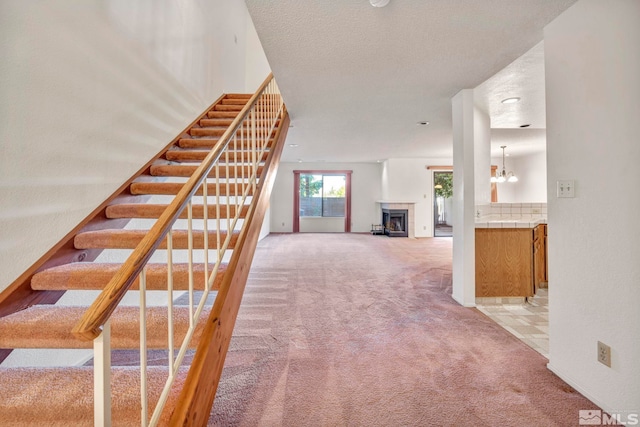 stairs with a fireplace, carpet, a textured ceiling, and an inviting chandelier