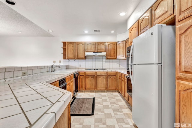 kitchen with tasteful backsplash, stainless steel oven, sink, white fridge, and tile counters