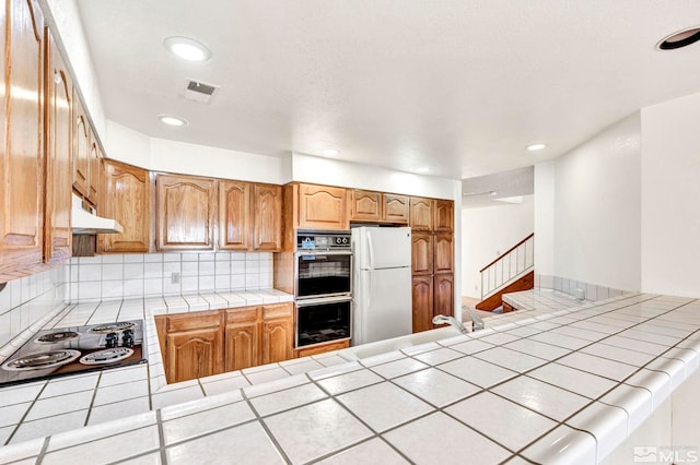 kitchen with backsplash, tile countertops, white fridge, and stainless steel gas stovetop