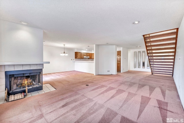 unfurnished living room featuring light carpet, a textured ceiling, an inviting chandelier, and a fireplace