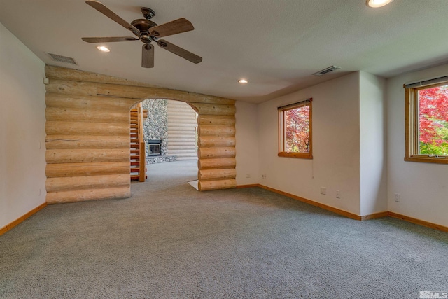 unfurnished room featuring carpet, ceiling fan, log walls, and a wealth of natural light