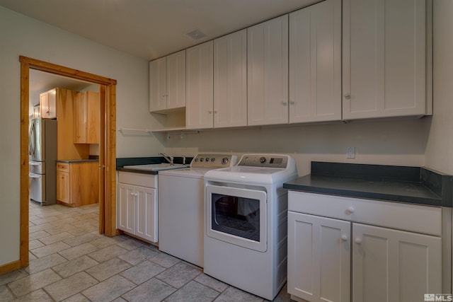 clothes washing area featuring washer and clothes dryer, sink, light tile floors, and cabinets