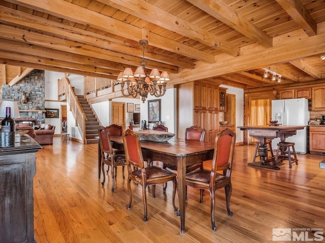 dining area featuring light hardwood / wood-style flooring, a fireplace, a notable chandelier, wooden ceiling, and beam ceiling