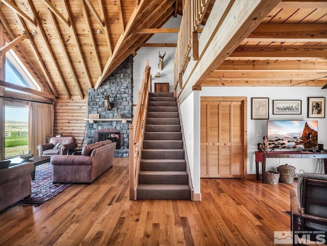 living room featuring wood-type flooring, a stone fireplace, rustic walls, and wood ceiling