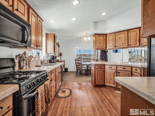 kitchen with light wood-type flooring, black appliances, a notable chandelier, sink, and lofted ceiling