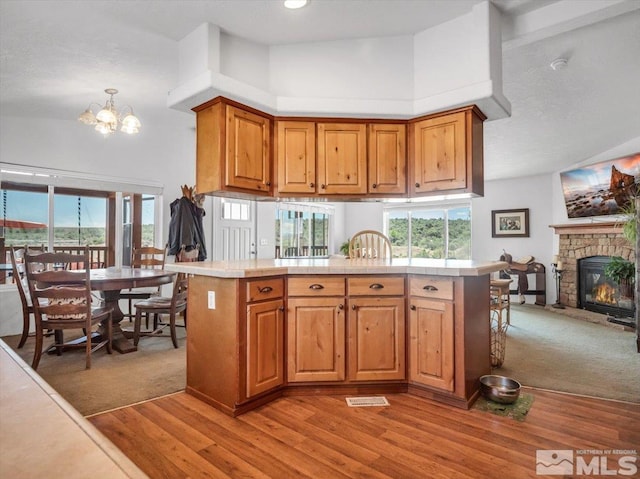 kitchen featuring a stone fireplace, hardwood / wood-style floors, kitchen peninsula, an inviting chandelier, and high vaulted ceiling