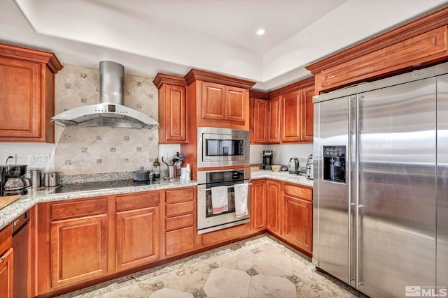 kitchen featuring built in appliances, light stone counters, backsplash, light tile floors, and wall chimney range hood