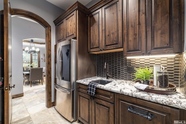 kitchen with light stone counters, light tile flooring, tasteful backsplash, stainless steel fridge, and sink